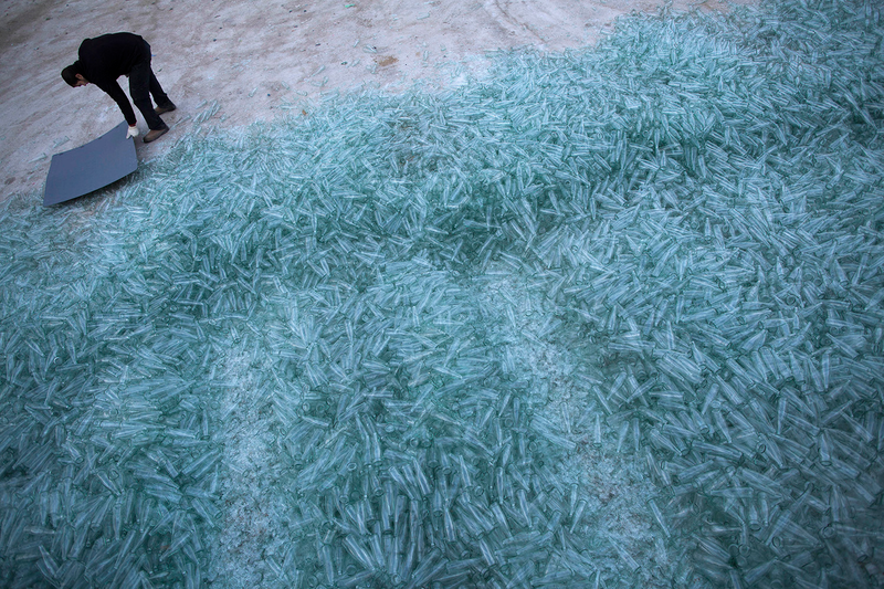 A worker breaks more clear glass bottles.